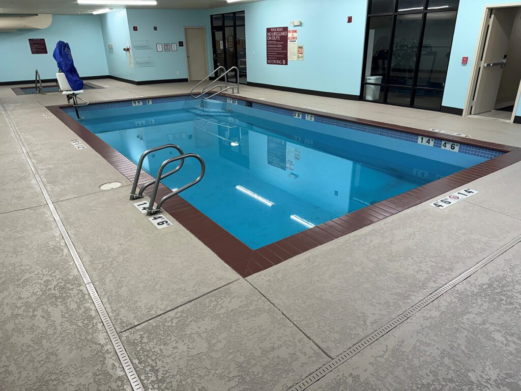 evergreen-1-reduced-texture-crete Indoor pool with brown tile border; photo facing pool entrance
